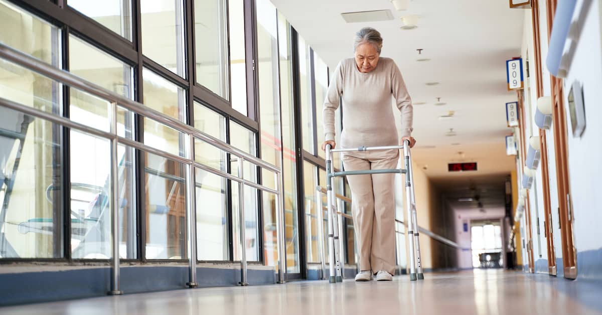 elderly woman with walker struggling to move down hall of a nursing home