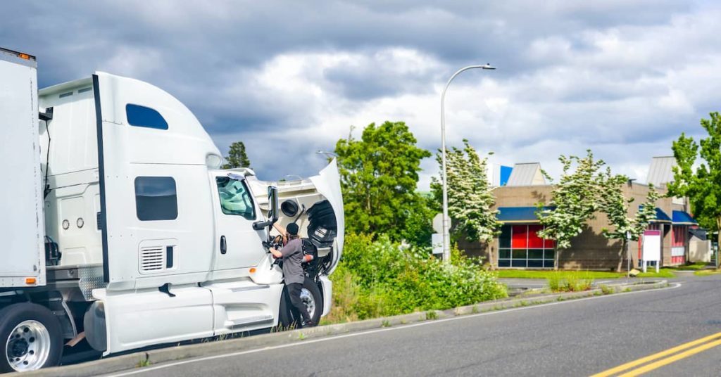 truck driver tending to the engine of a semi-truck cab broken down on the side of the road