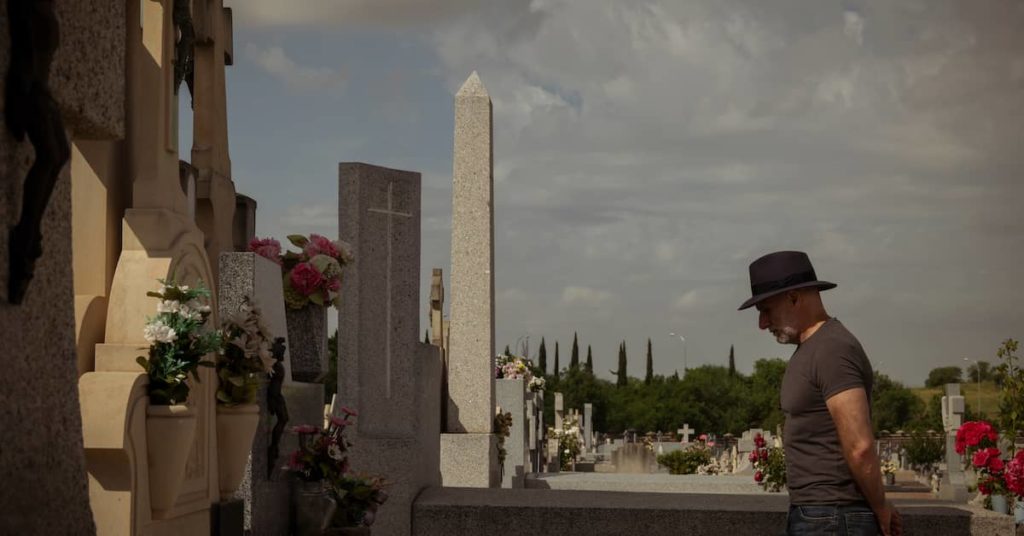 man in a cemetery bowing his head at the grave of a departed loved one