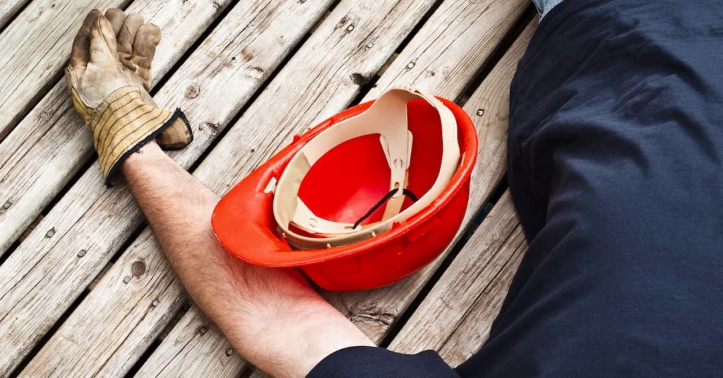injured male worker lying next to his hardhat on wood floorboards Columbus work injury lawyer