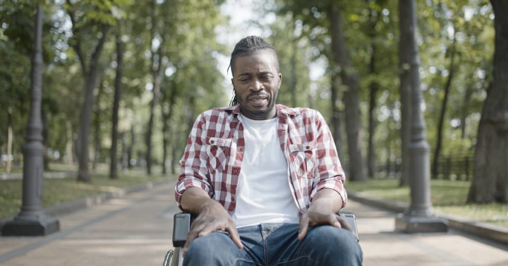 man sitting in wheelchair in park upset about his injury