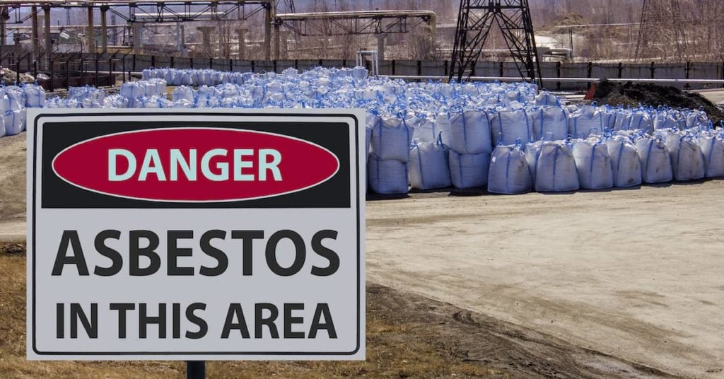 Danger: Asbestos in This Area sign at industrial site with bags of asbestos waste