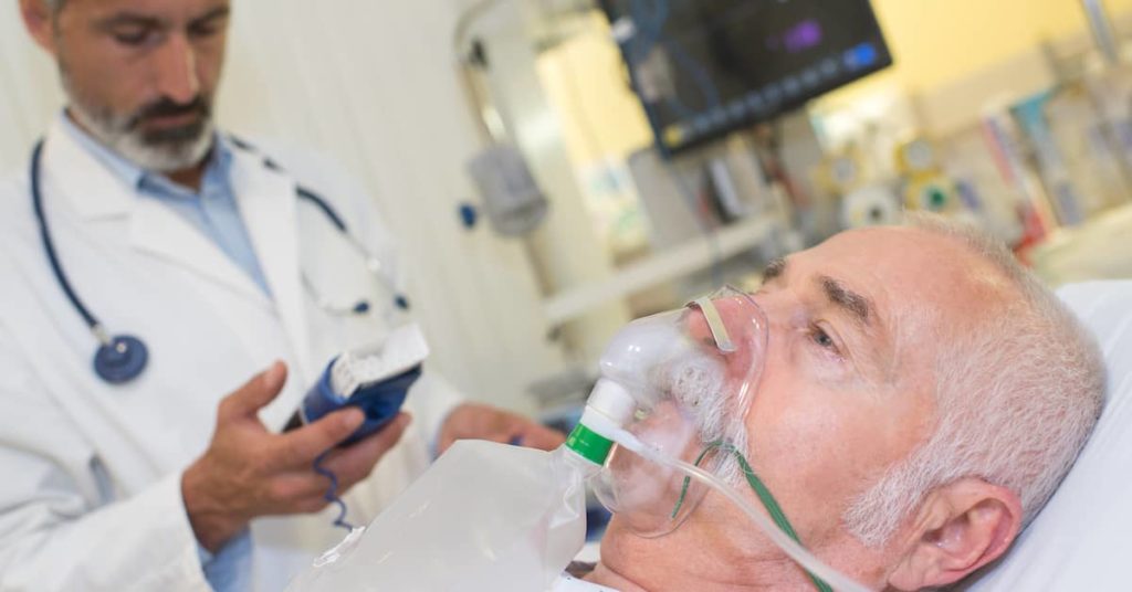 male mesothelioma patient with oxygen mask receiving treatment from doctor in hospital