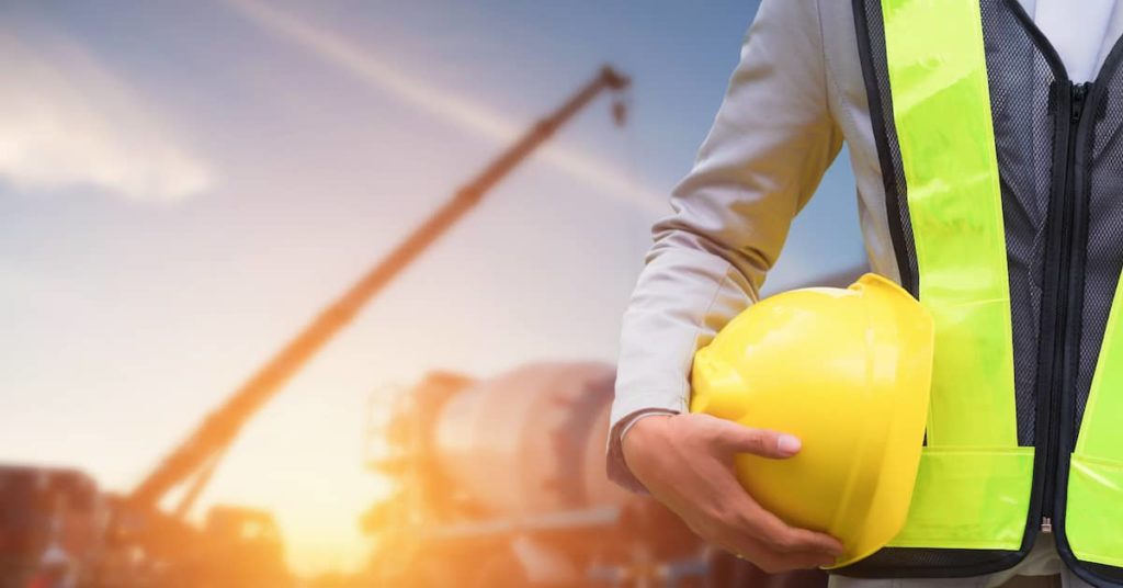 engineer holding hard hat standing in front of construction equipment on job site