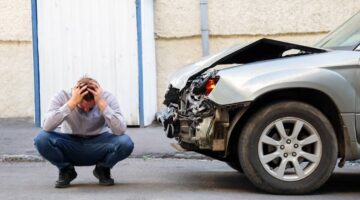Man injured in car accident holding his head next to the wrecked vehicle | Colombo Law