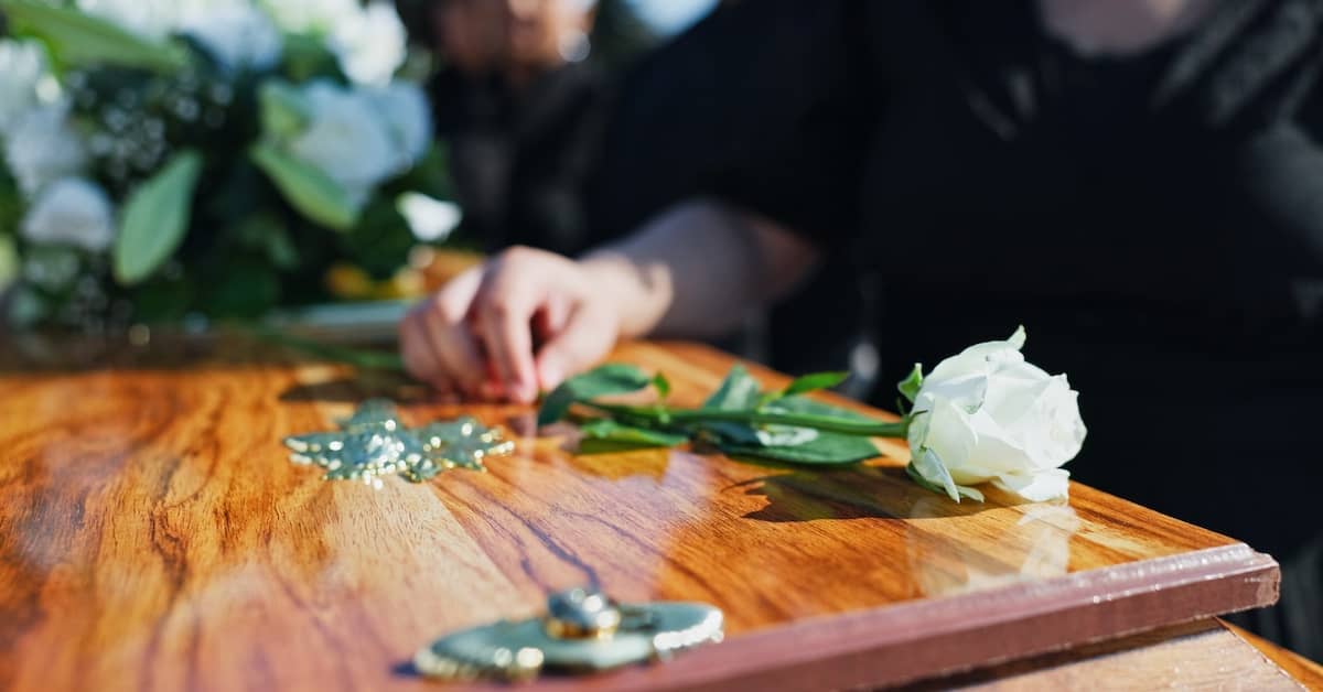 Woman laying a white rose on the coffin of a deceased loved on | Colombo Law
