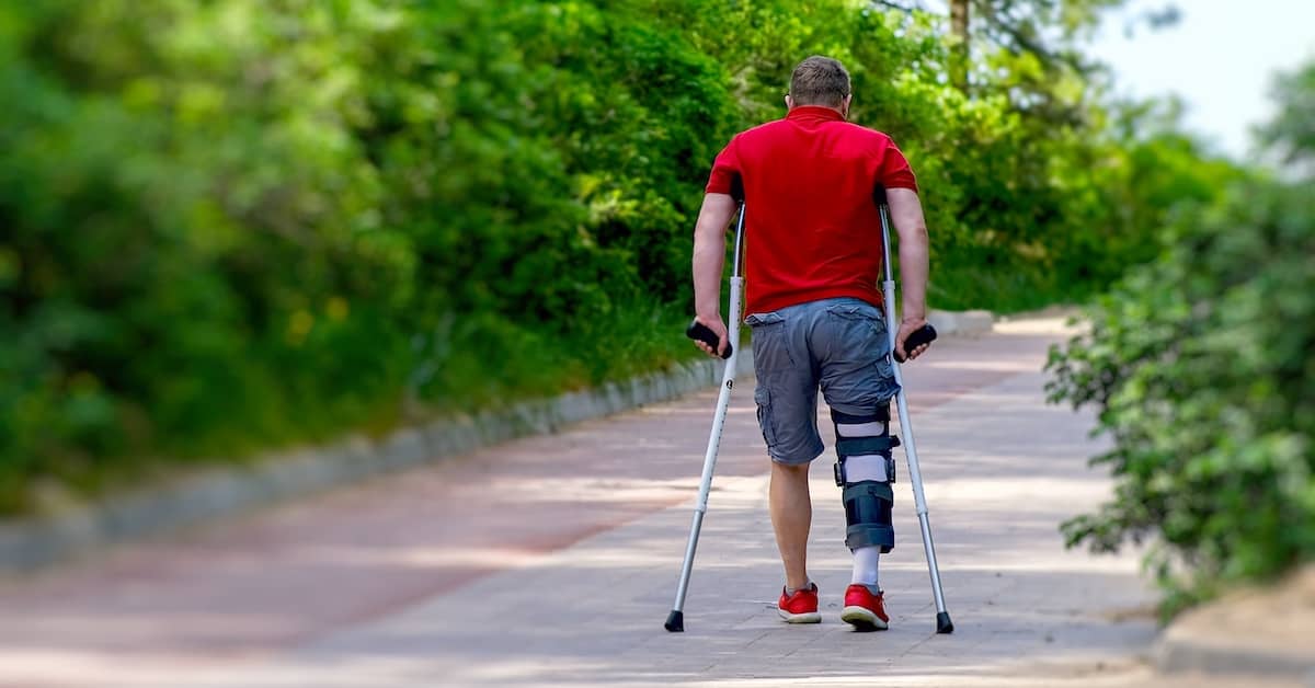 Injured man walking down the sidewalk with crutches and a leg brace | Colombo Law
