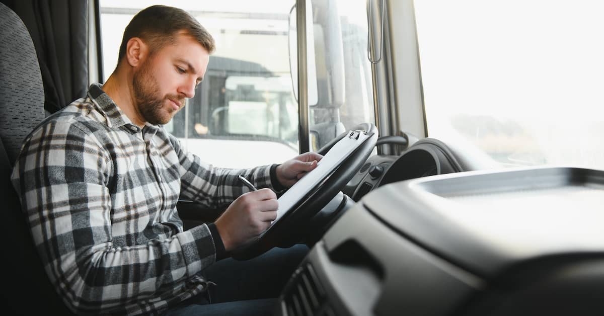 Truck driver filling out paperwork in the cab of his truck | Colombo Law